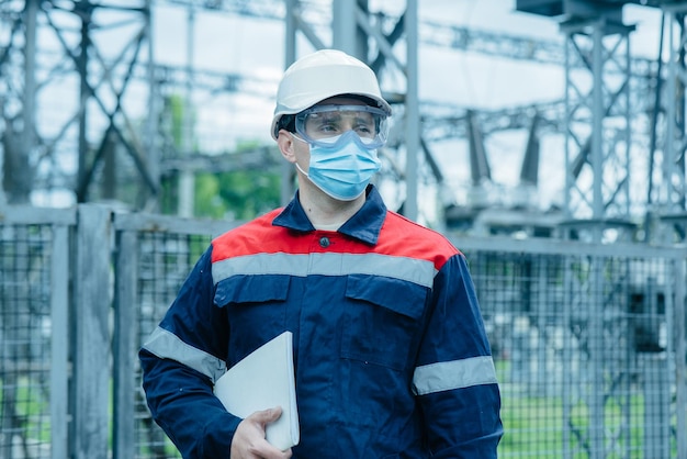 Энергетик в маске во время пандемии осматривает современное оборудование электроподстанции перед вводом в эксплуатацию Энергетика и промышленность Плановый ремонт электрооборудования