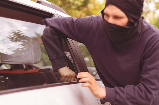 覆面をした泥棒が車の窓のロックを解除して開き、財産を盗む
