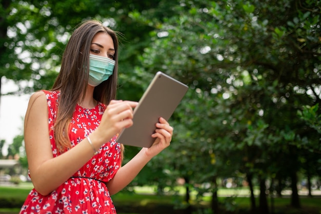 Masked woman using a tablet in the park