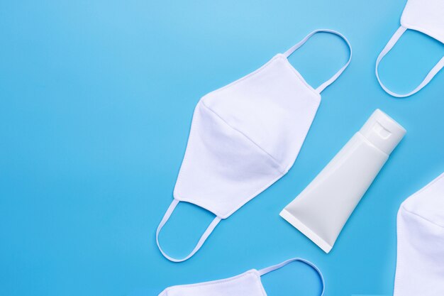 Maskers en alcohol handdesinfecterende gel in witte glanzende plastic buis voor bescherming van het hygiënecoronavirus (Covid-19). Blauwe achtergrond