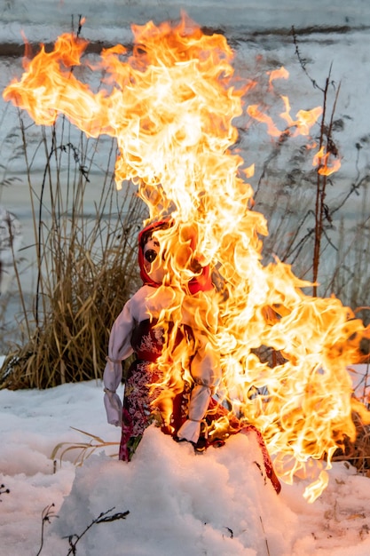 Maslenitsa-pop branden op sneeuw in het gedroogde gras