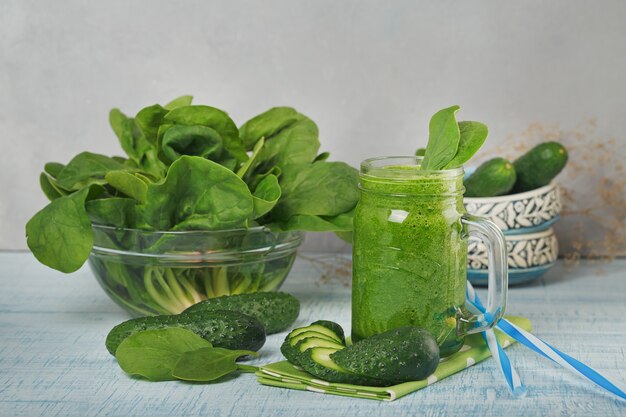 Mason jar mokken gevuld met verse groene spinazie en komkommer smoothie op lichtblauwe houten ondergrond. Gezond eten en vegetarisch concept.