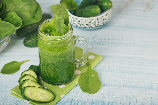 Mason jar mokken gevuld met verse groene spinazie en komkommer smoothie op lichtblauwe houten ondergrond. gezond eten en vegetarisch concept.