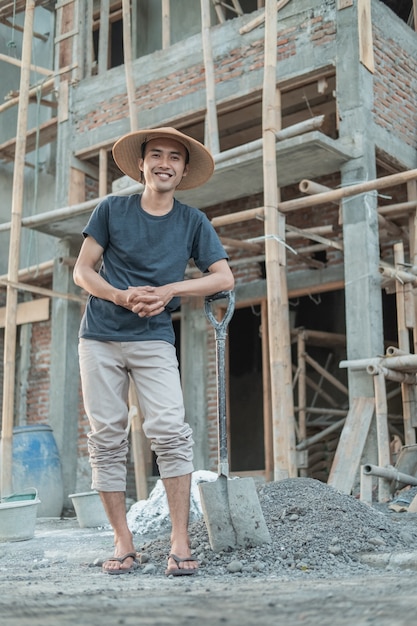 家の建設でシャベルを持って立っているときに笑顔の帽子をかぶった石工