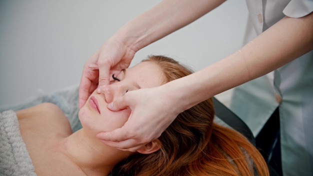 Massage  omassage therapist massaging the face of a redhaired woman with her hands