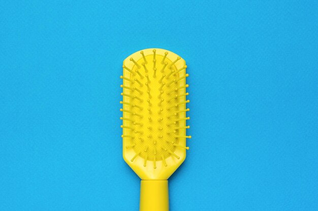 Massage plastic yellow comb on a blue background Minimal hair care concept