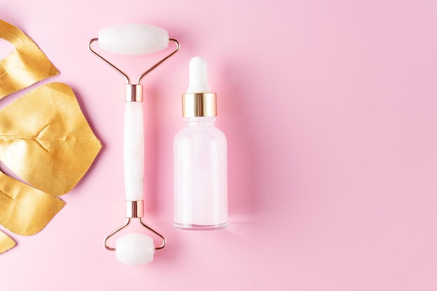 Massage quartz roller and pink glass bottle of cosmetic liquid\
transparent serum on pink background. dropper bottle, hyaluronic\
acid, oil, serum. facial massage and relaxation. gua sha massage\
tools.