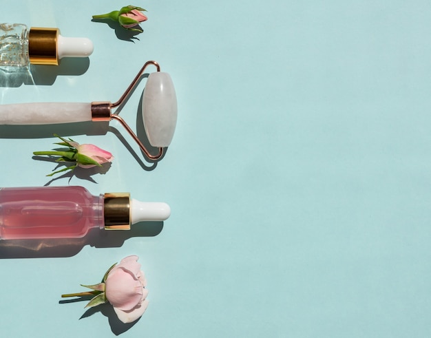 Photo massage roller for face made of rose quartz with bottles of cosmetic oil or serum on blue background