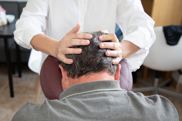 Massage therapist man massaging male head skull sitting on massage seated by woman specialist on knee massage chair adapted seat