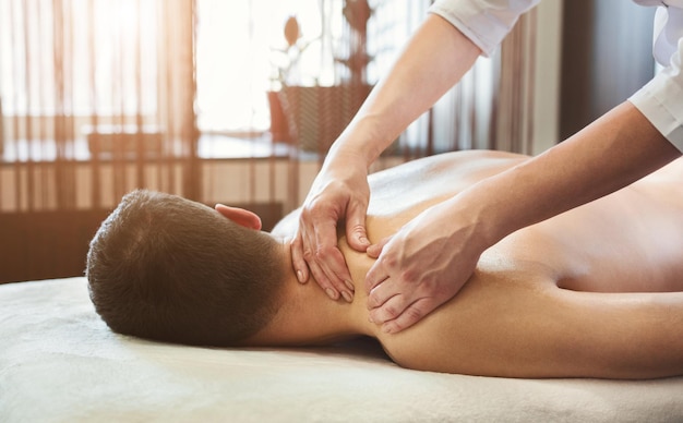 Massage therapist massaging male shoulders in spa center