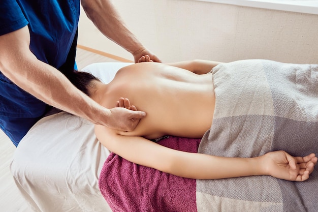 Photo massage therapist uses backs of his hands to massage upper back in shoulder area as he presses on