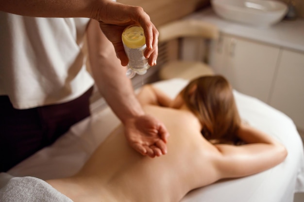 Massagetherapeut brengt aromatische olie aan op zijn hand voordat hij de vrouw masseert