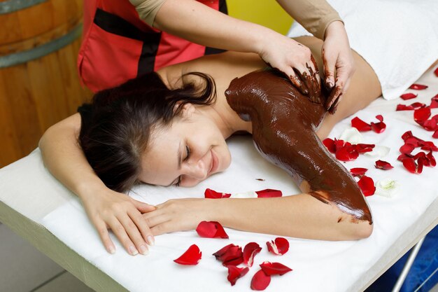 Masseur die chocolade op de rug van de vrouw toepast. Massage in de spa salon