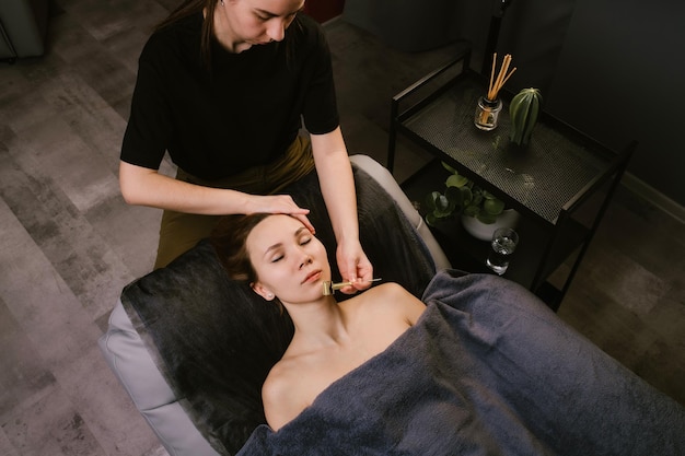 Masseur die vrouwentempelmassage geeft in een schoonheidssalon met een getipte roller