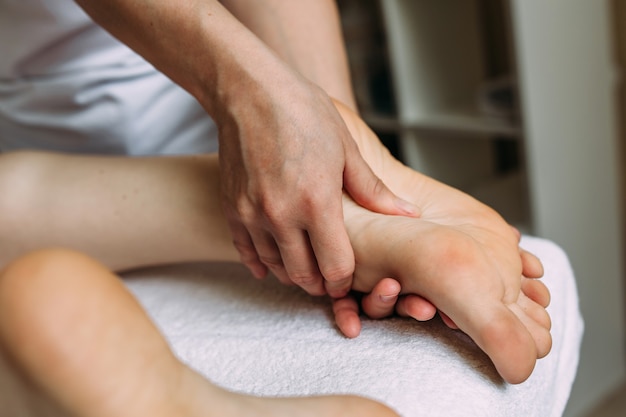 The masseur gives a massage to the female feet at the spa