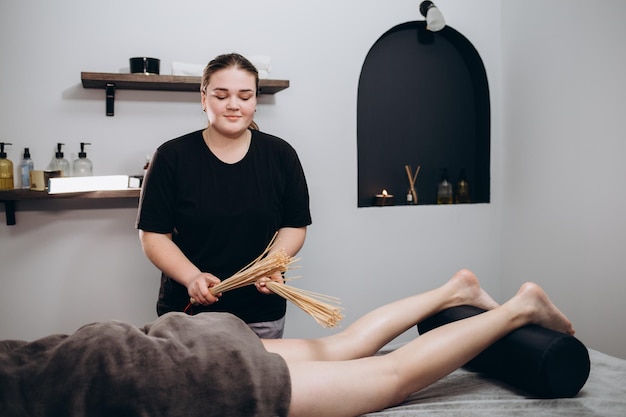 Masseur makes massage to young girl Woman having bamboo stick massage at day spa