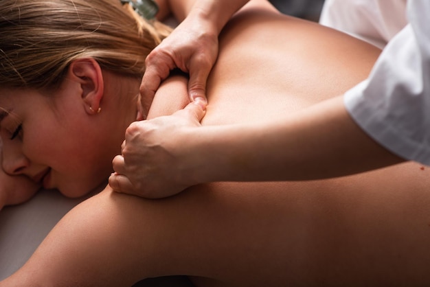 Masseur massaging back and shoulder blades of young woman on massage table Concept of massage spa treatments Closeup