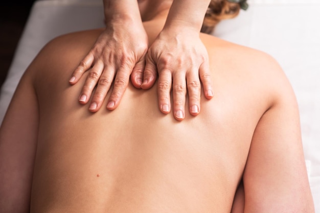 Masseur masseert rug- en schouderbladen van jonge vrouw op massagetafel Concept van massage spa-behandelingen Close-up