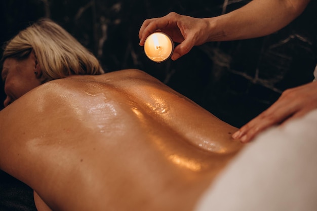 Photo masseur woman drips wax from a candle on the back of the young girl rubbing massage oil relaxation before the holidays