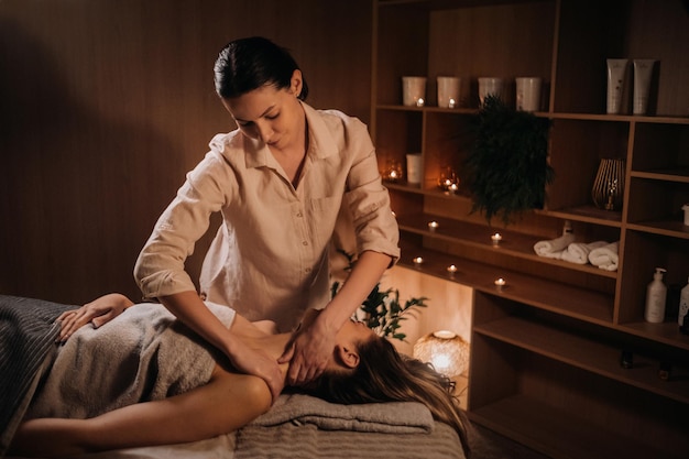 A masseuse gives a body massage to a woman in a spa center A professional masseur massages the shoulder of a girl lying in a spa center