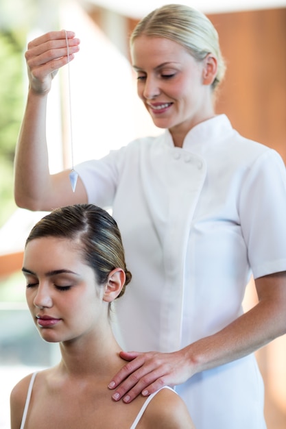 Masseuse holding pendant over woman head