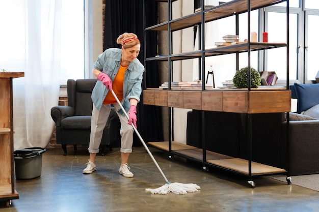 Massive cleaning session. Active fit adult woman in bright outfit meticulously washing floor with long mop