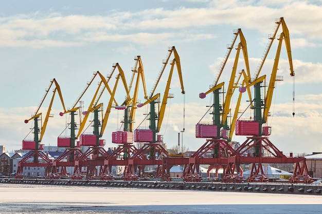Massive harbor cranes in seaport. Heavy load dockside cranes in port, cargo container yard, container ship terminal. Business and commerce, logistics. Winter industrial scene.
