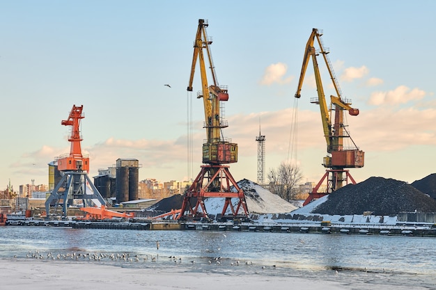 Massive harbor cranes in seaport. Heavy load dockside cranes in port, cargo container yard, container ship terminal. Business and commerce, logistics. Winter industrial scene.