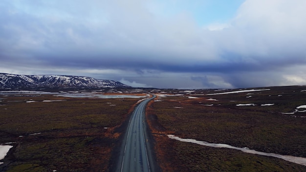 Massive roads between snowy mountains and frozen fields in iceland, drone shot of icelandic roadside with beautiful landscapes. Scandinavian scenic route with hills, winter scenery.