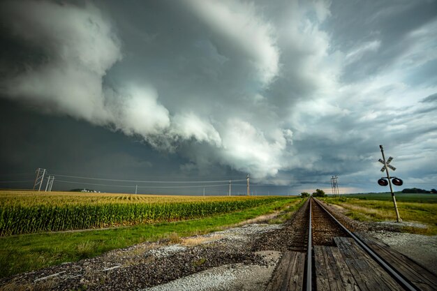 Photo massive tornado looms in the distance over the illinois railroad track