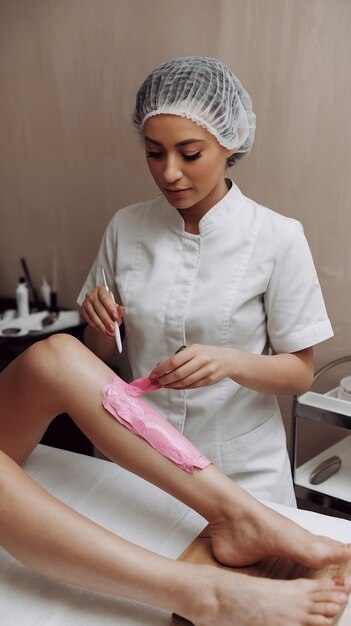 Photo a master applies pink depilatory wax to a young womans leg for hr removal depilation with wax