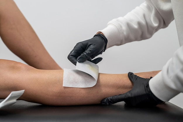 Master applies wax for depilation on the leg of a young woman to remove hair with a cartridge