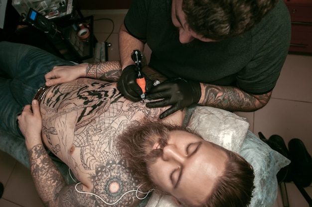 Master of the art of tattooing working on professional tattoo machine device in the salon.