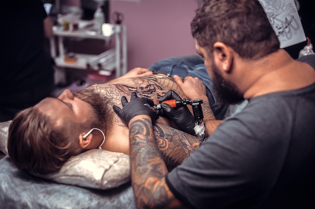 Master of the art of tattooing working on professional tattoo machine gun in tattoo parlour.