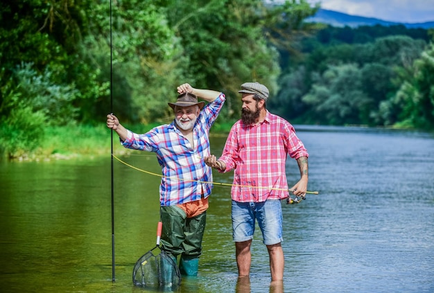 Master baiter Fisherman with fishing rod Activity and hobby Fishing freshwater lake pond river Bearded men catching fish Mature man with friend fishing Summer vacation Happy cheerful people