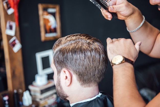 The master in the barbershop shaves and cuts the man in front of the mirror