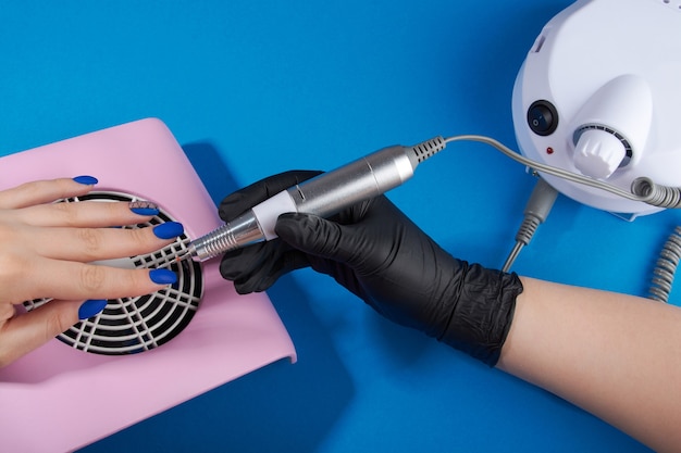 A master in black gloves does a manicure on a blue background