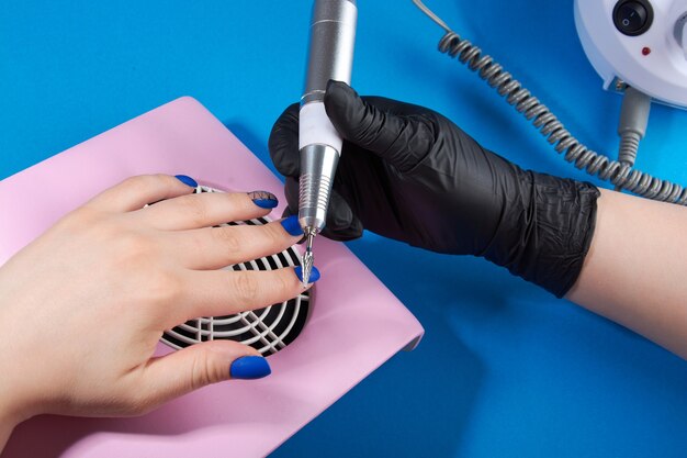 A master in black gloves does a manicure on a blue background