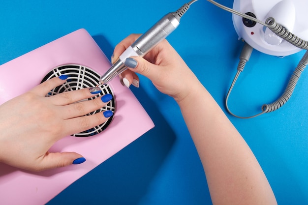 A master in black gloves does a manicure on a blue background