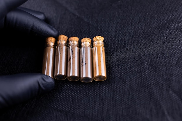 A master in black gloves holds bottles of henna for eyebrow coloring in front of him