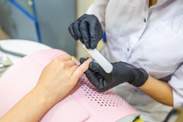 The master in black gloves in the salon makes manicure pedicure to the client