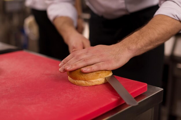 マスターシェフがレストランのキッチンでハンバーガーのロールを切る