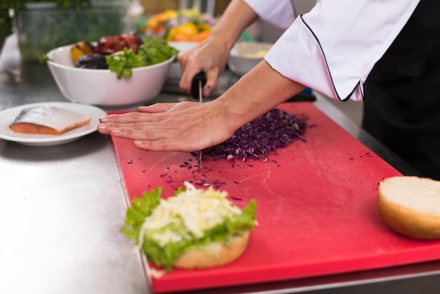 Il maestro chef taglia l'insalata per un hamburger nella cucina del ristorante