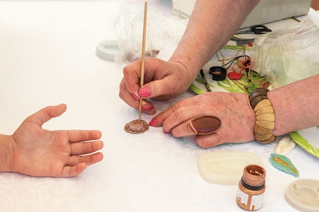 Master class in jewelry making A woman teaches a child to make a brooch with an inscription