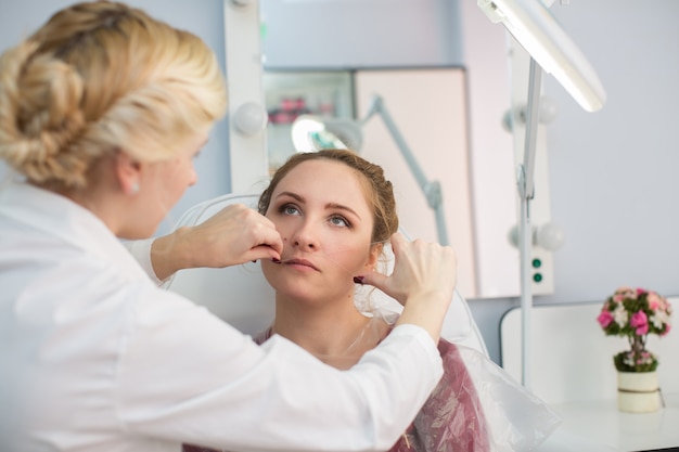 Master corrigeert make-up, geeft vorm en draad plukt wenkbrauwen in een schoonheidssalon. professionele verzorging voor het gezicht