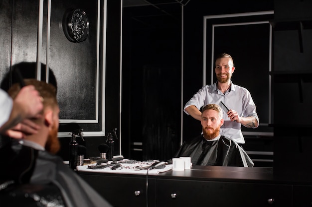 Фото Мастер стрижет волосы и бороду в парикмахерской
