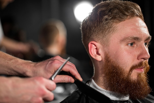 Master cuts hair and beard in the Barber shop. Hairdresser makes hairstyle using scissors and a metal comb