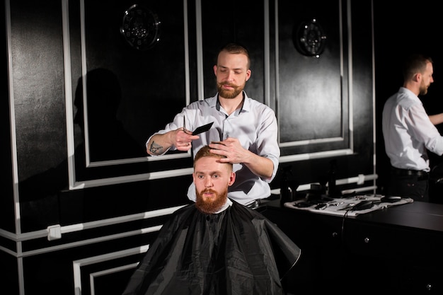 Master cuts hair and beard in the Barber shop. Hairdresser makes hairstyle using scissors and a metal comb