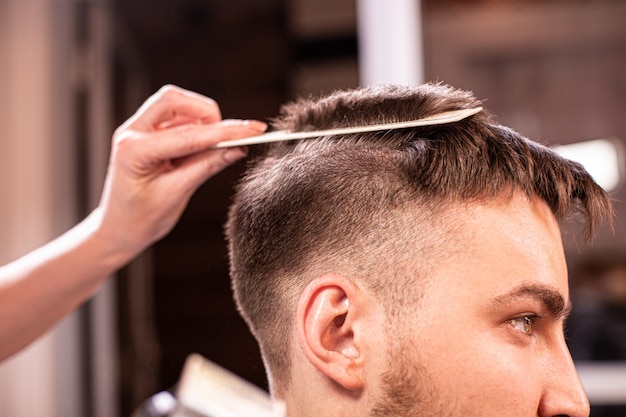 The master cuts the hair and beard of a man in a barbershop, a hairdresser does a haircut for a young man. Beauty concept, self care.