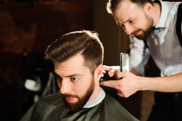 Il maestro taglia i capelli e la barba degli uomini nel barbiere